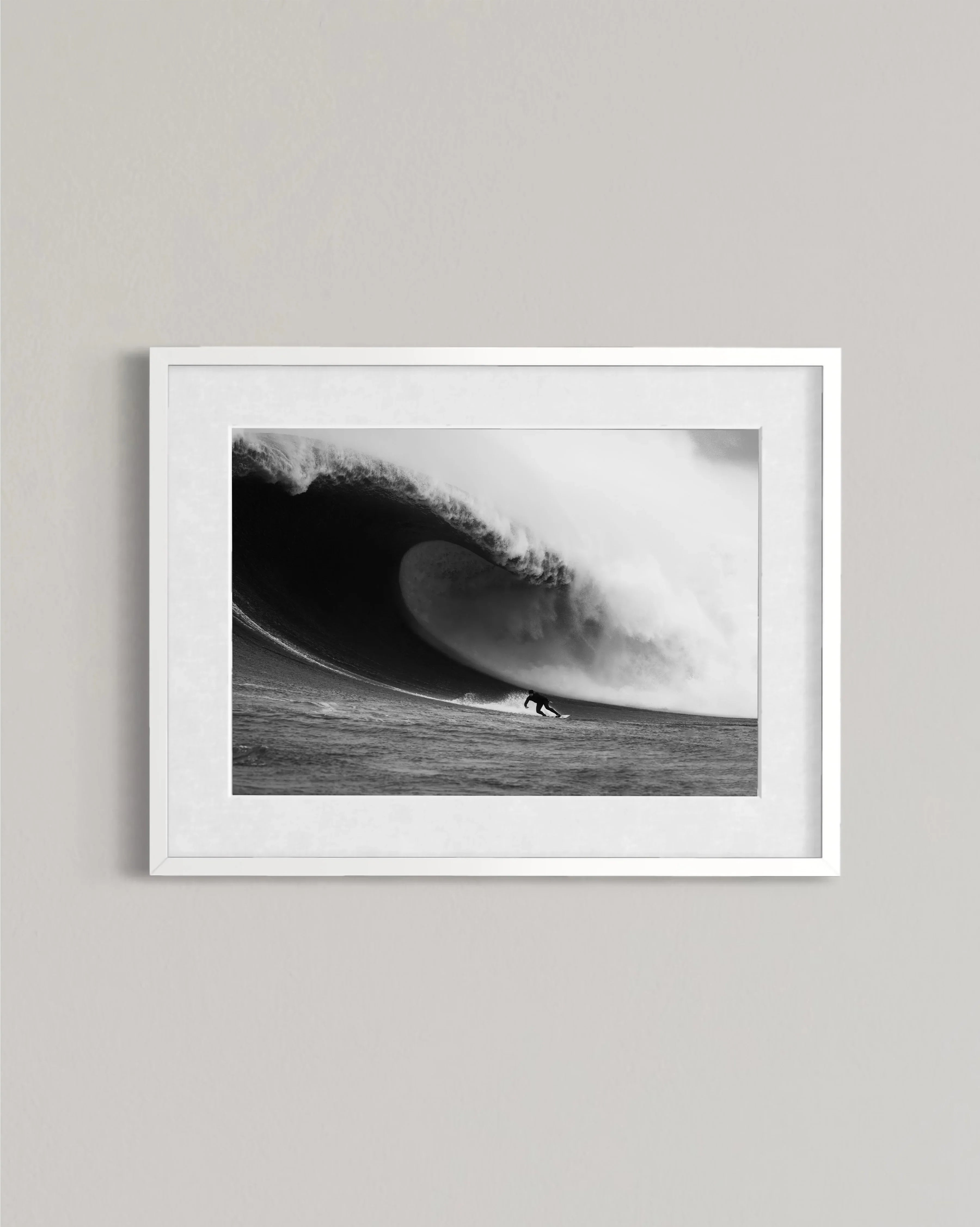 Black and white photo of surfer riding a large breaking wave displayed in a white frame on a gray wall