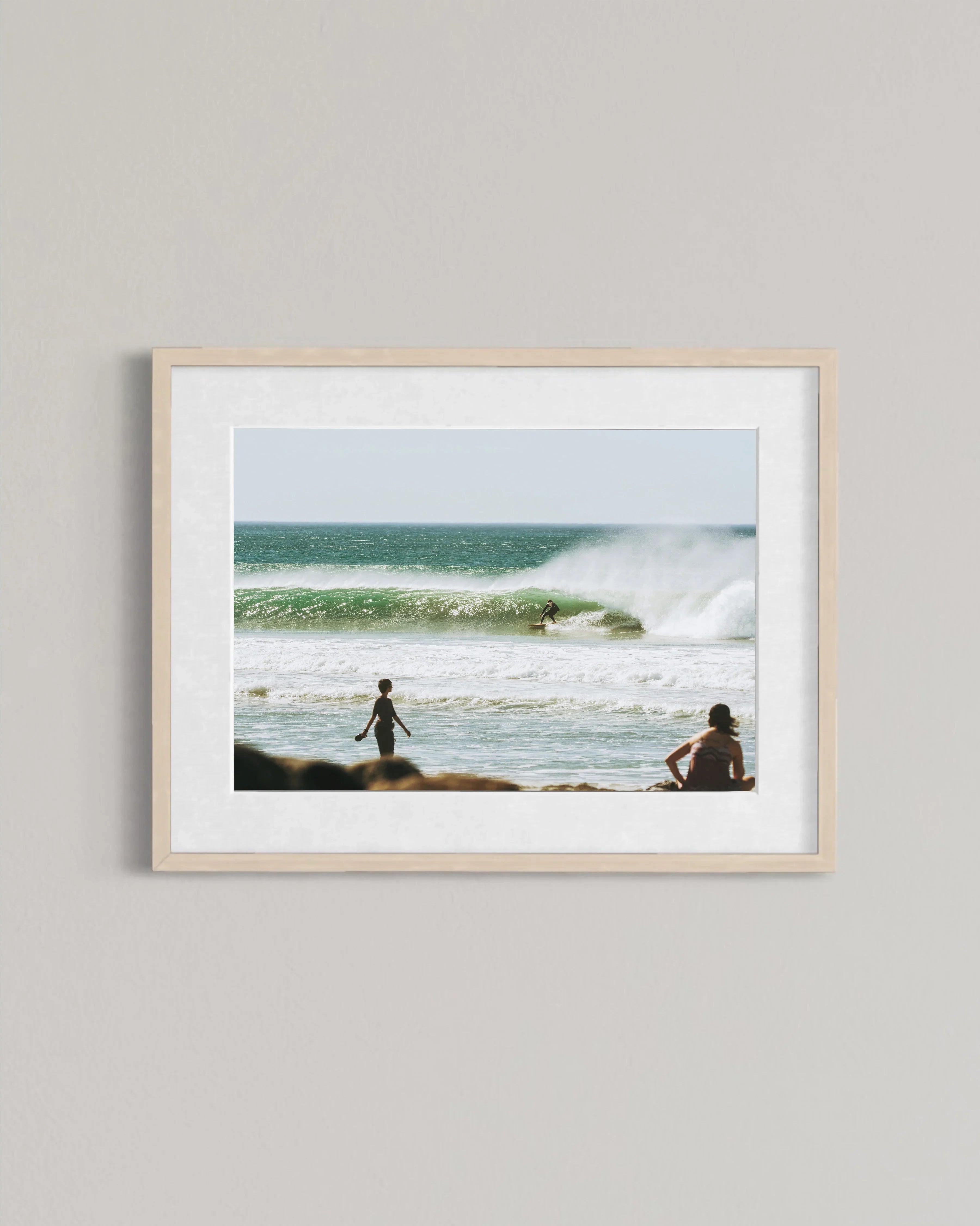 Framed photo of ocean waves with surfer riding a wave and two people watching from shore