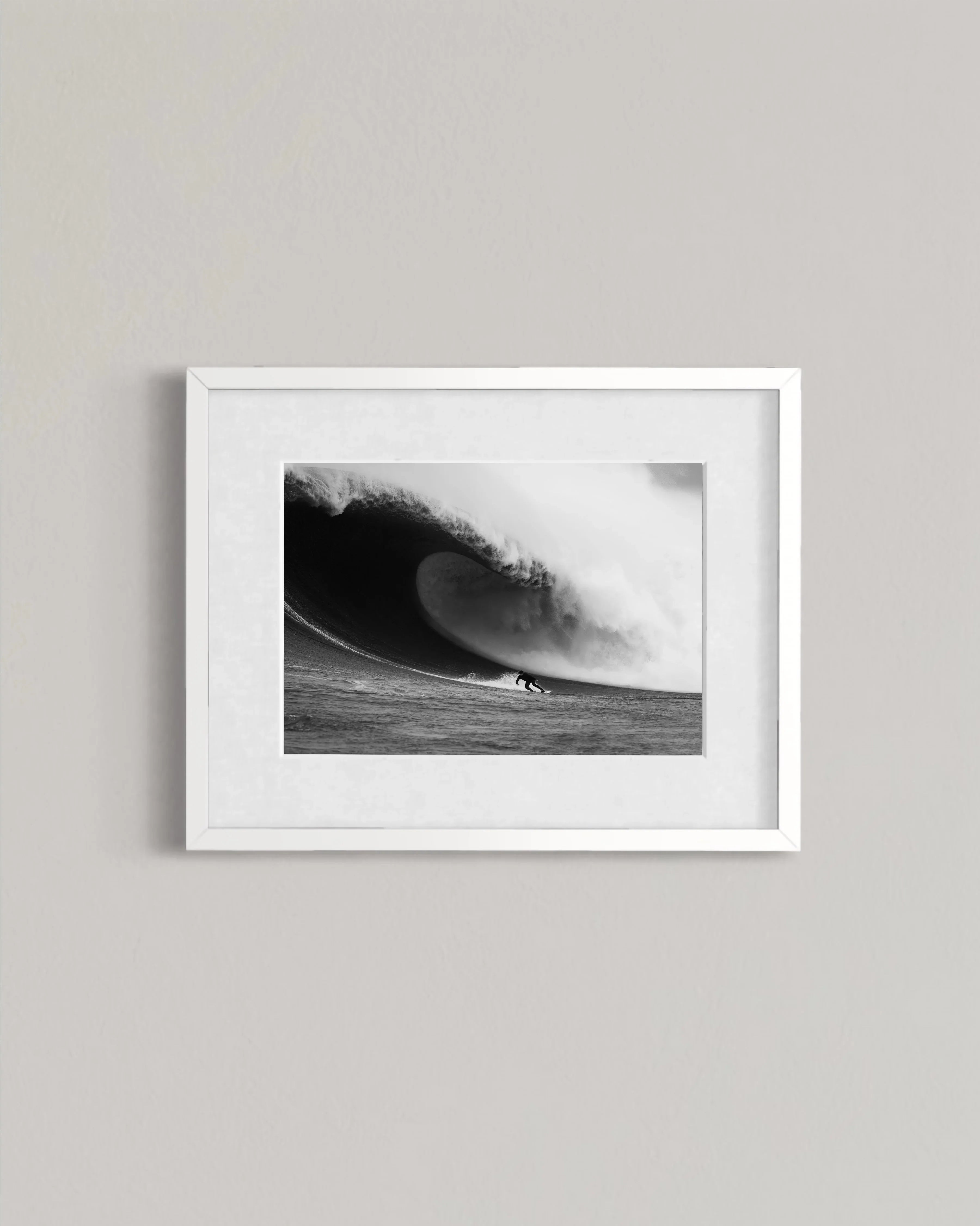 Black and white framed photo of surfer riding large curling wave on ocean