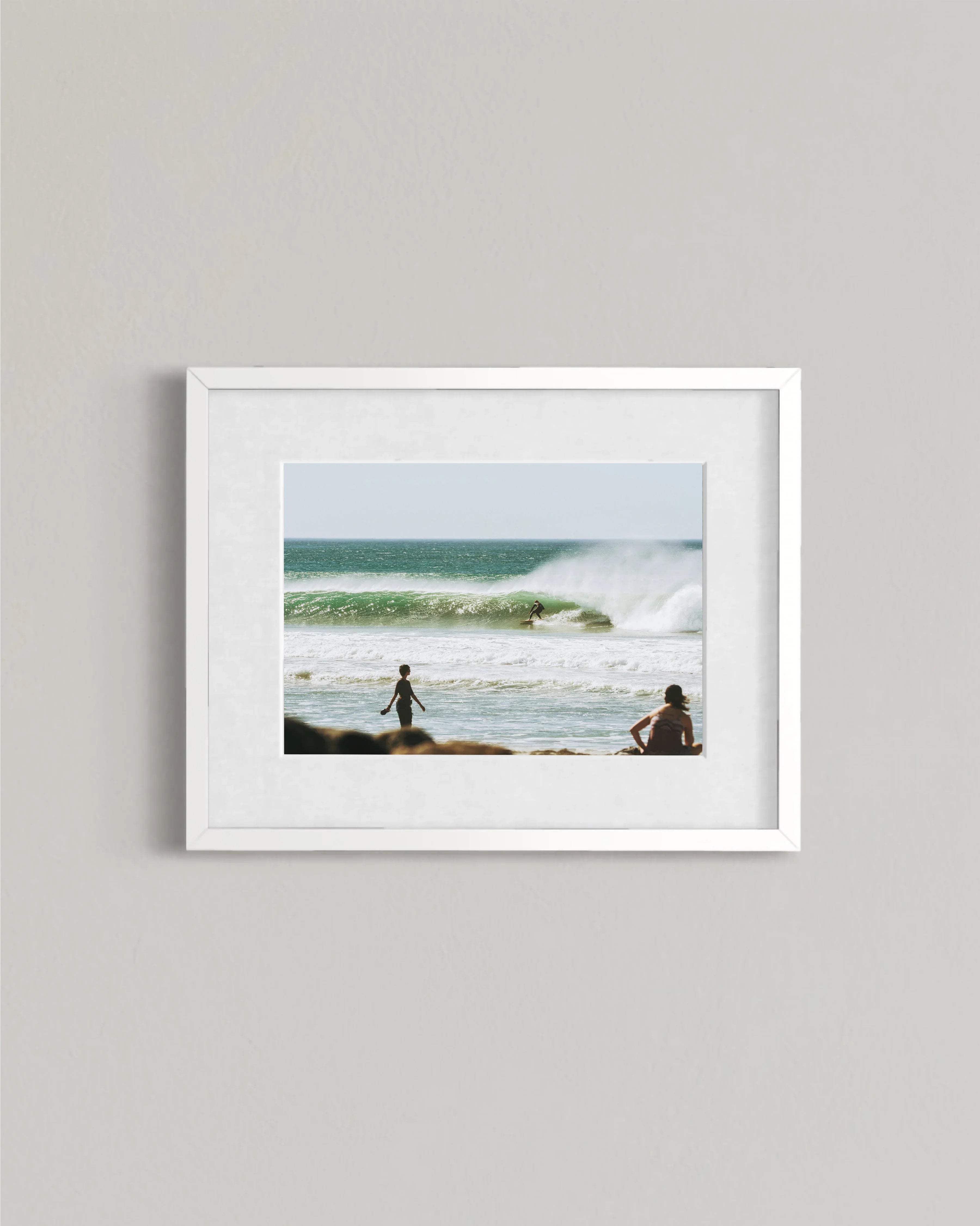 Framed photo of surfer riding ocean wave with two people watching from the beach