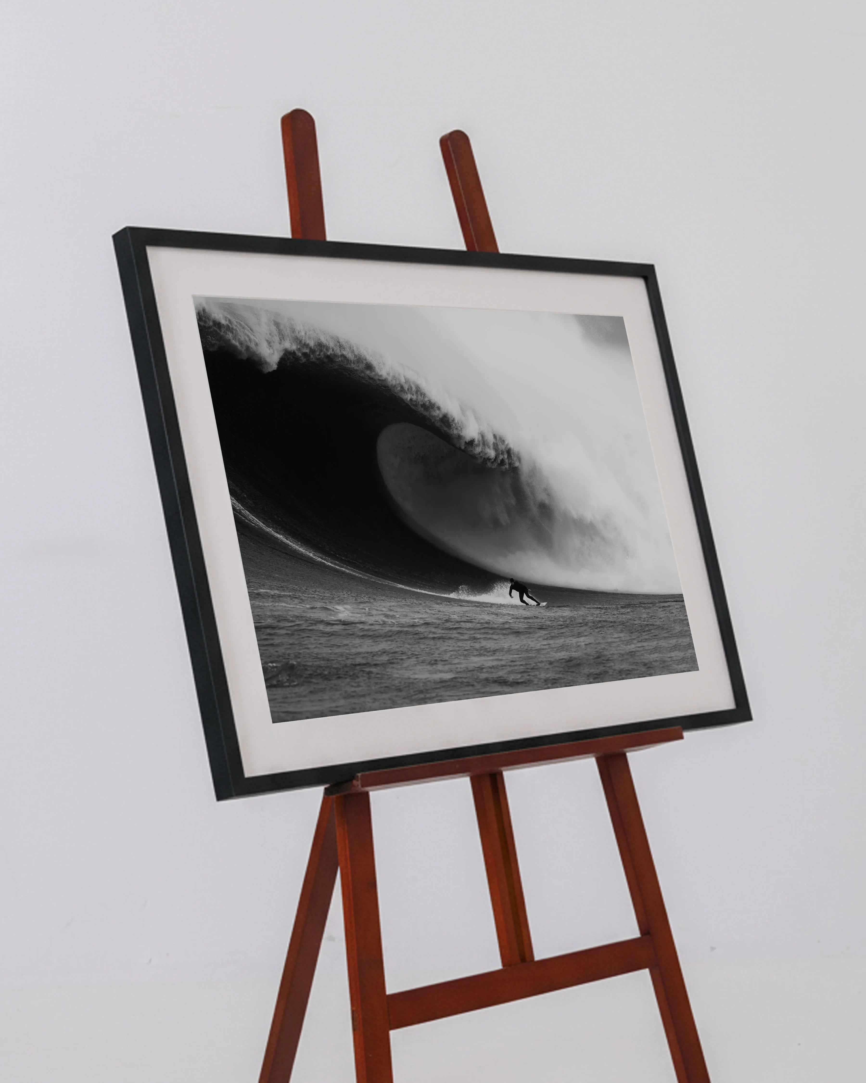 Black and white framed photo of a surfer riding a huge curling wave on a wooden easel