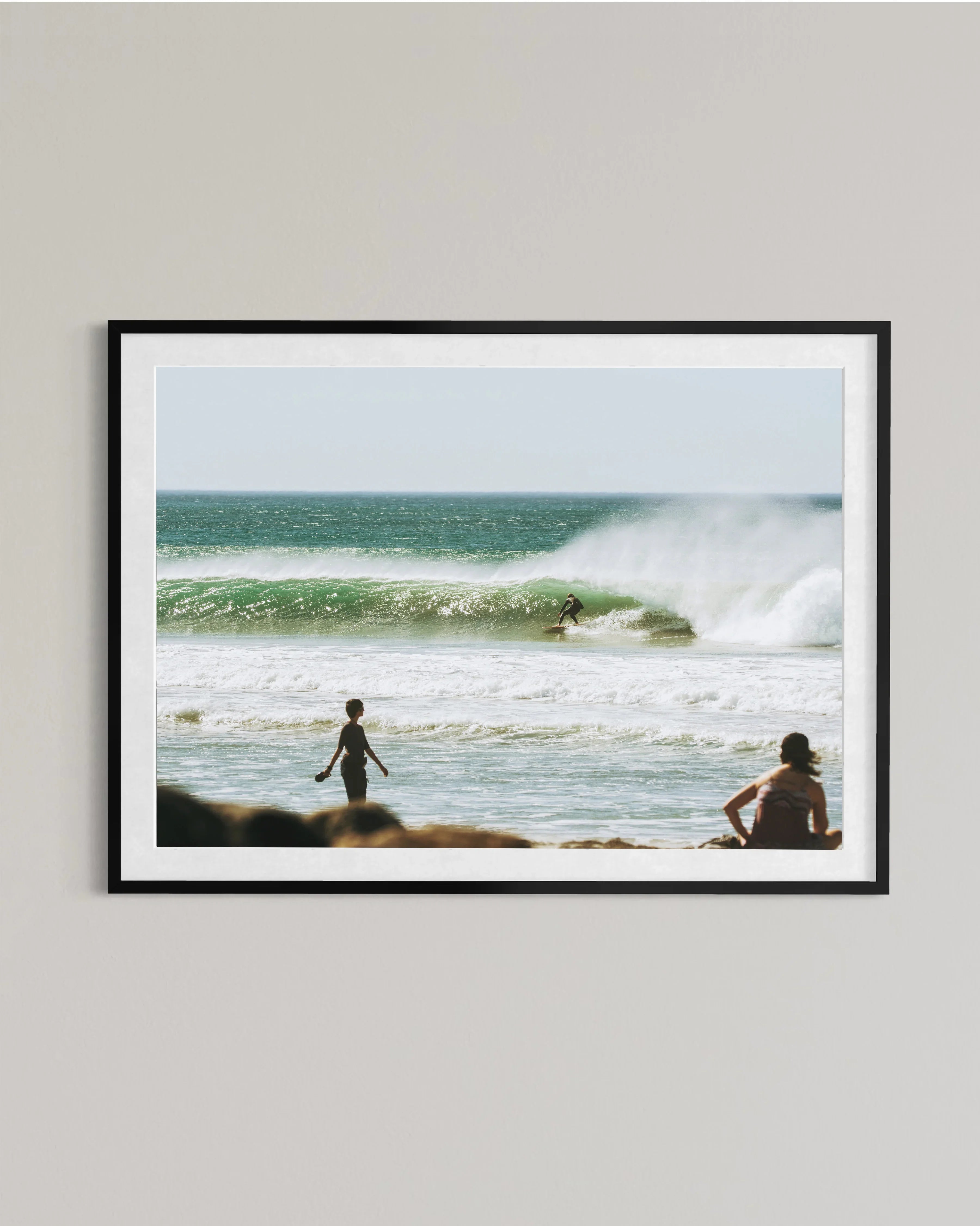 Framed photo of a surfer riding a large wave with two people watching from the beach