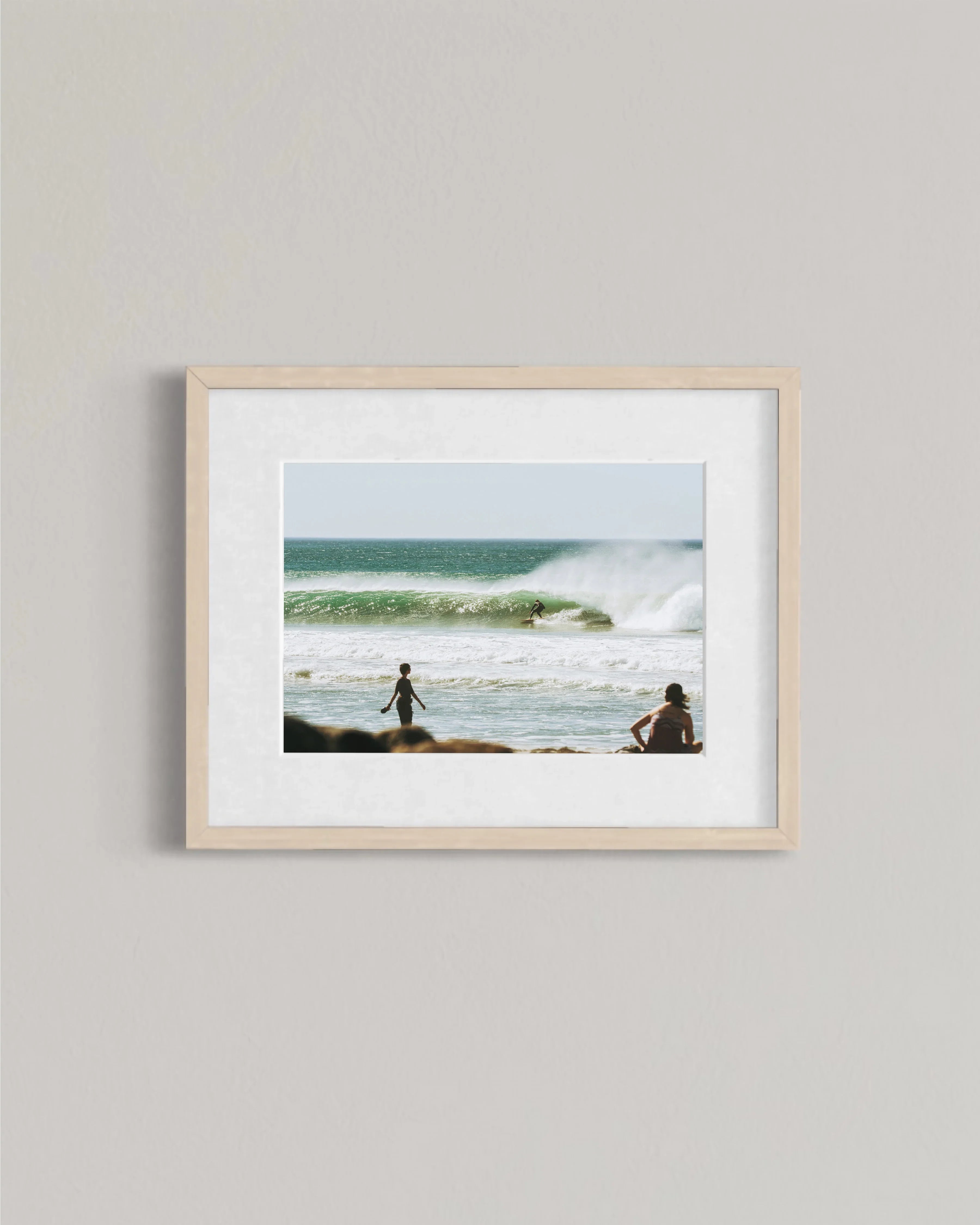 Framed photo of surfer riding wave with two people watching on beach shore