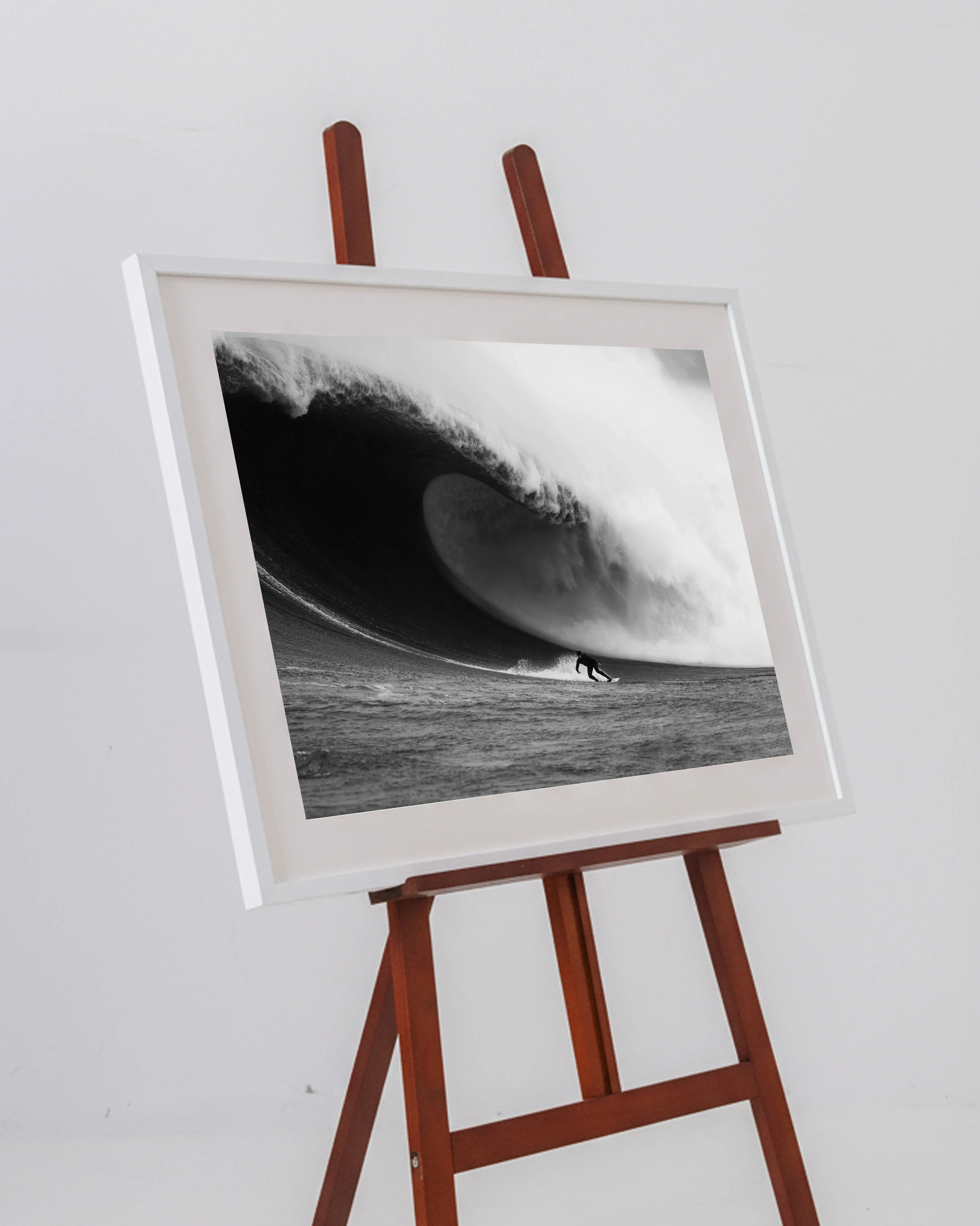 Black and white photo of a surfer riding a large wave, framed and displayed on a wooden easel