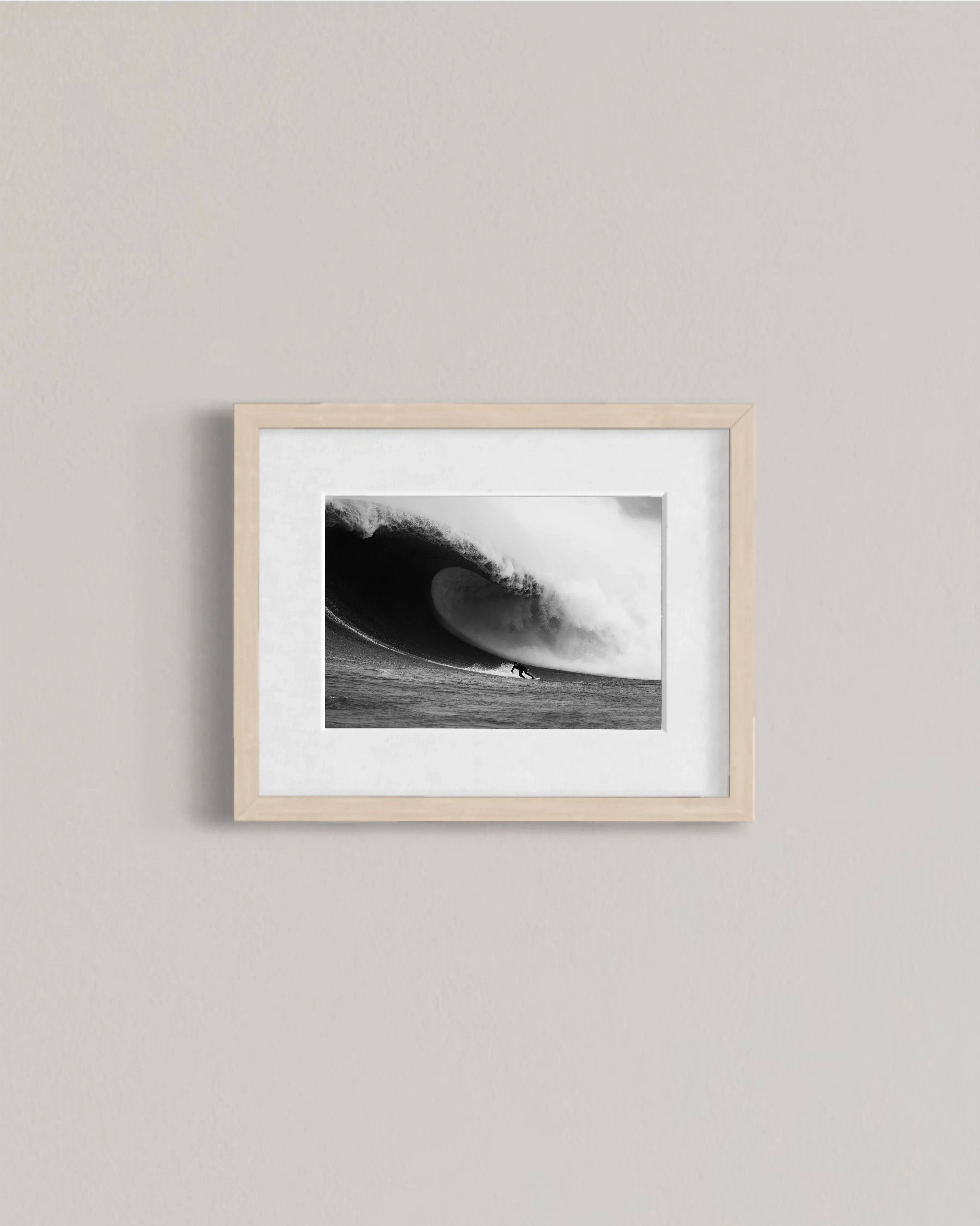 Framed black and white photo of surfer riding a large curling wave on a light wall