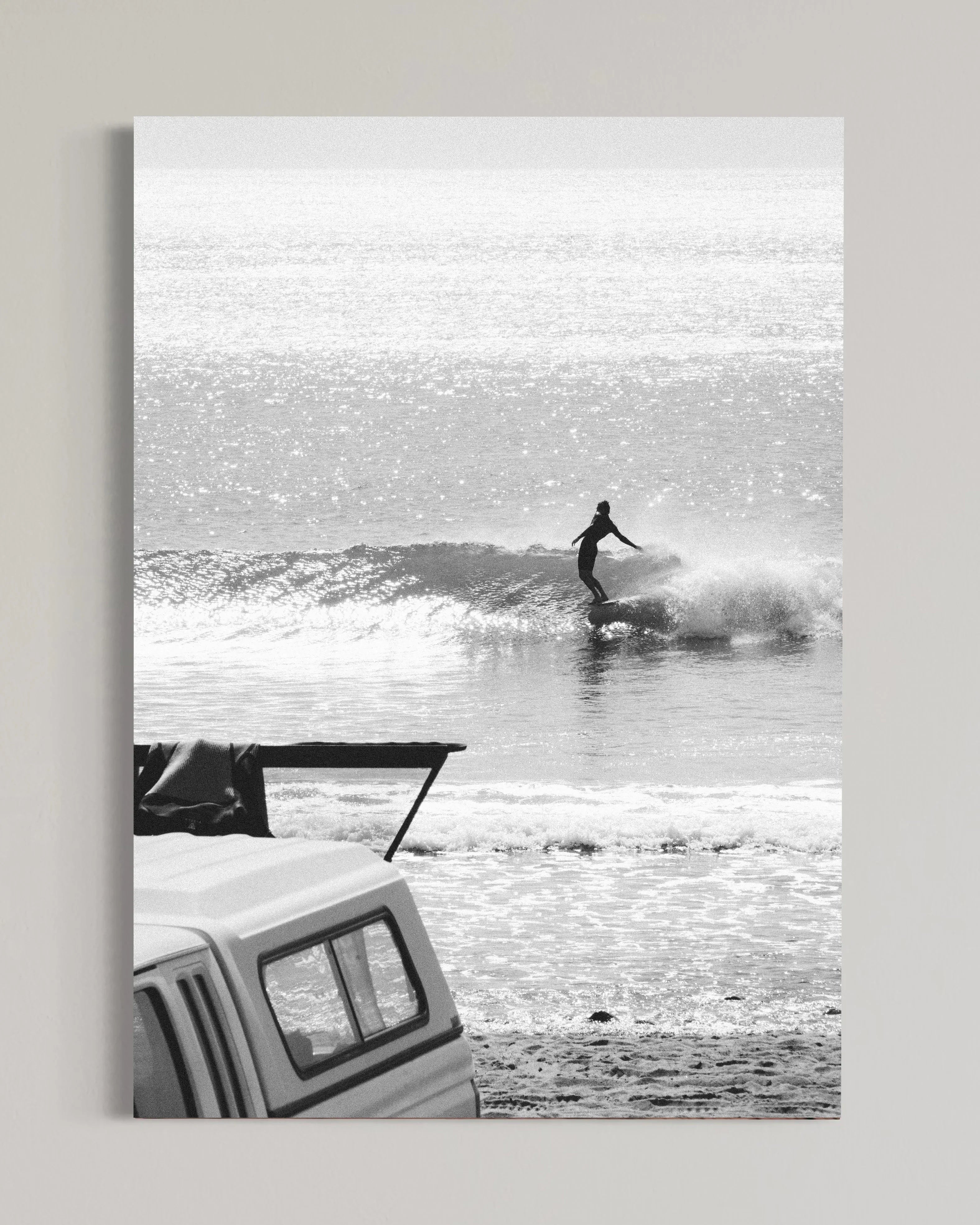 Black and white photo of surfer riding a wave near the shore with a parked truck on the beach