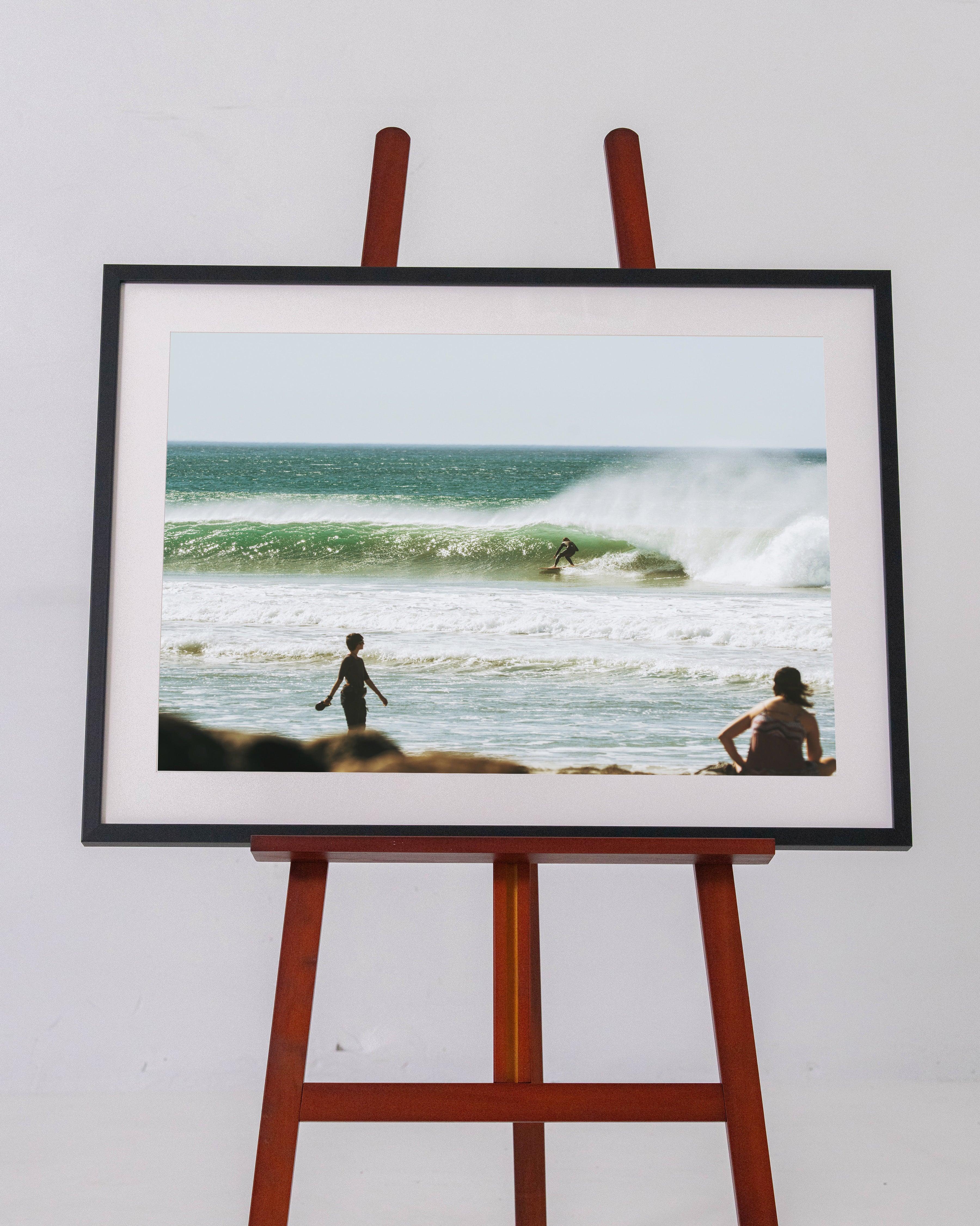 Framed photo of surfer riding green wave at beach with two people watching from shore