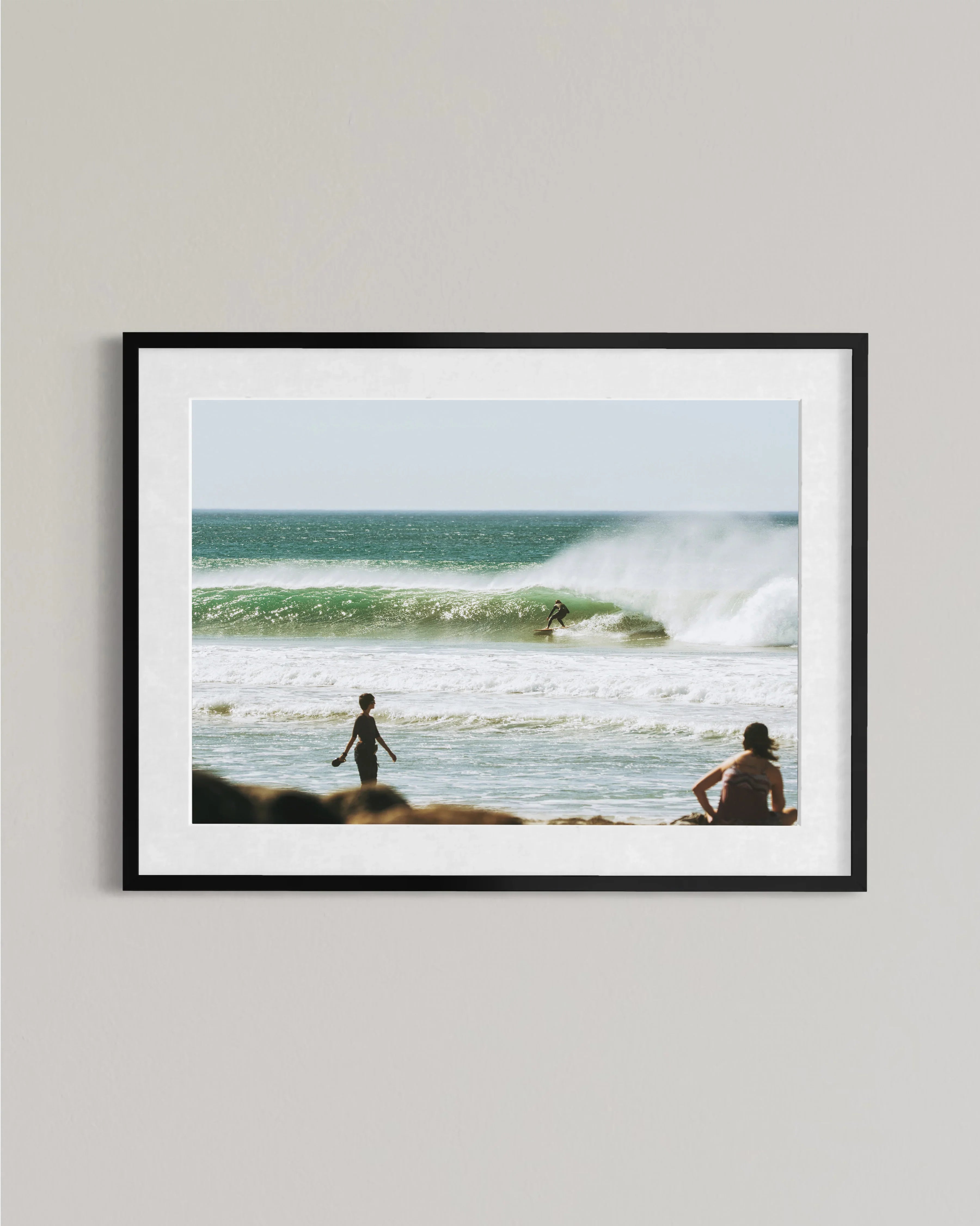 Framed photo of surfer riding green wave at sunny beach with two people watching from shore