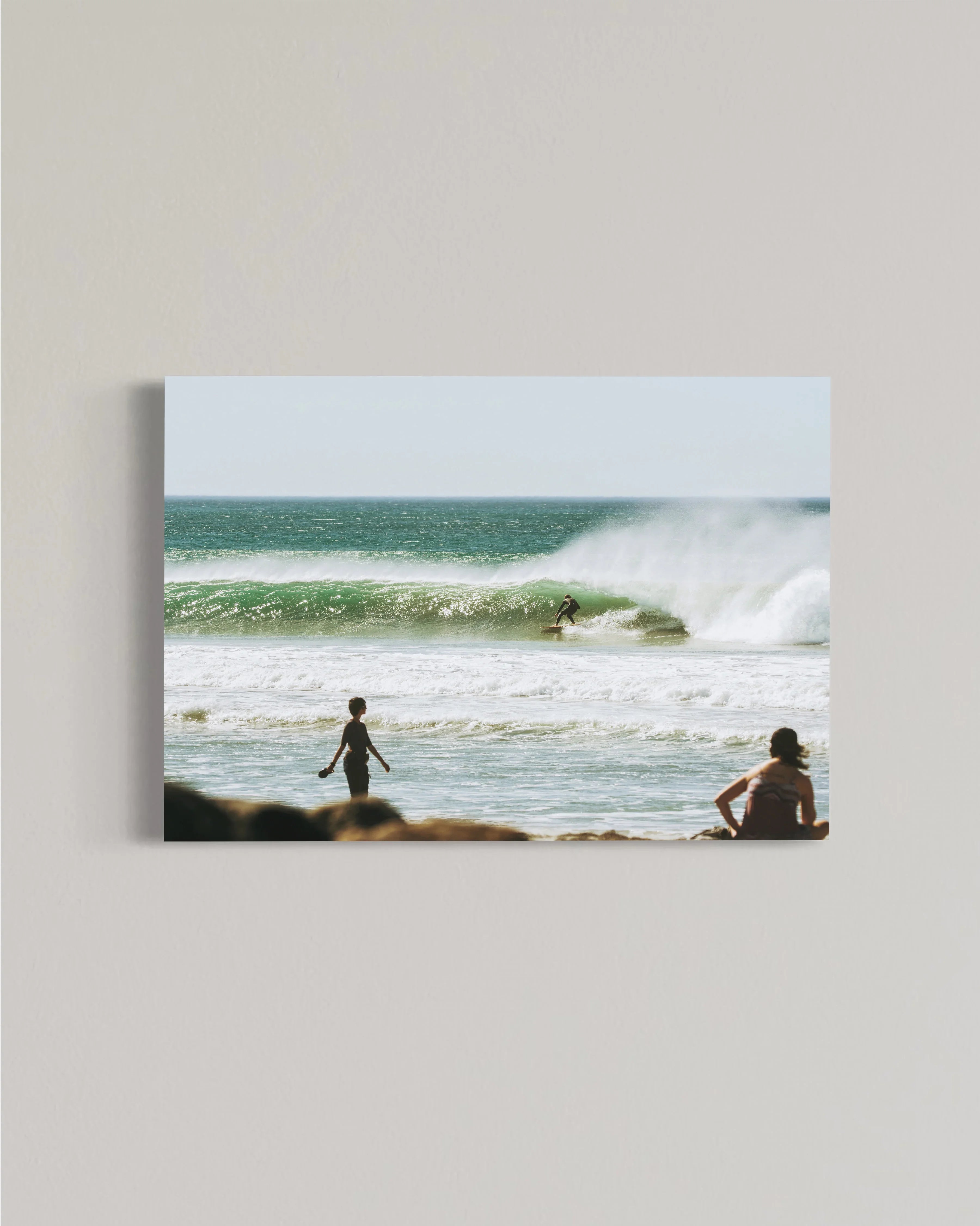 Surfer riding a large wave in the ocean with two people watching from sandy beach