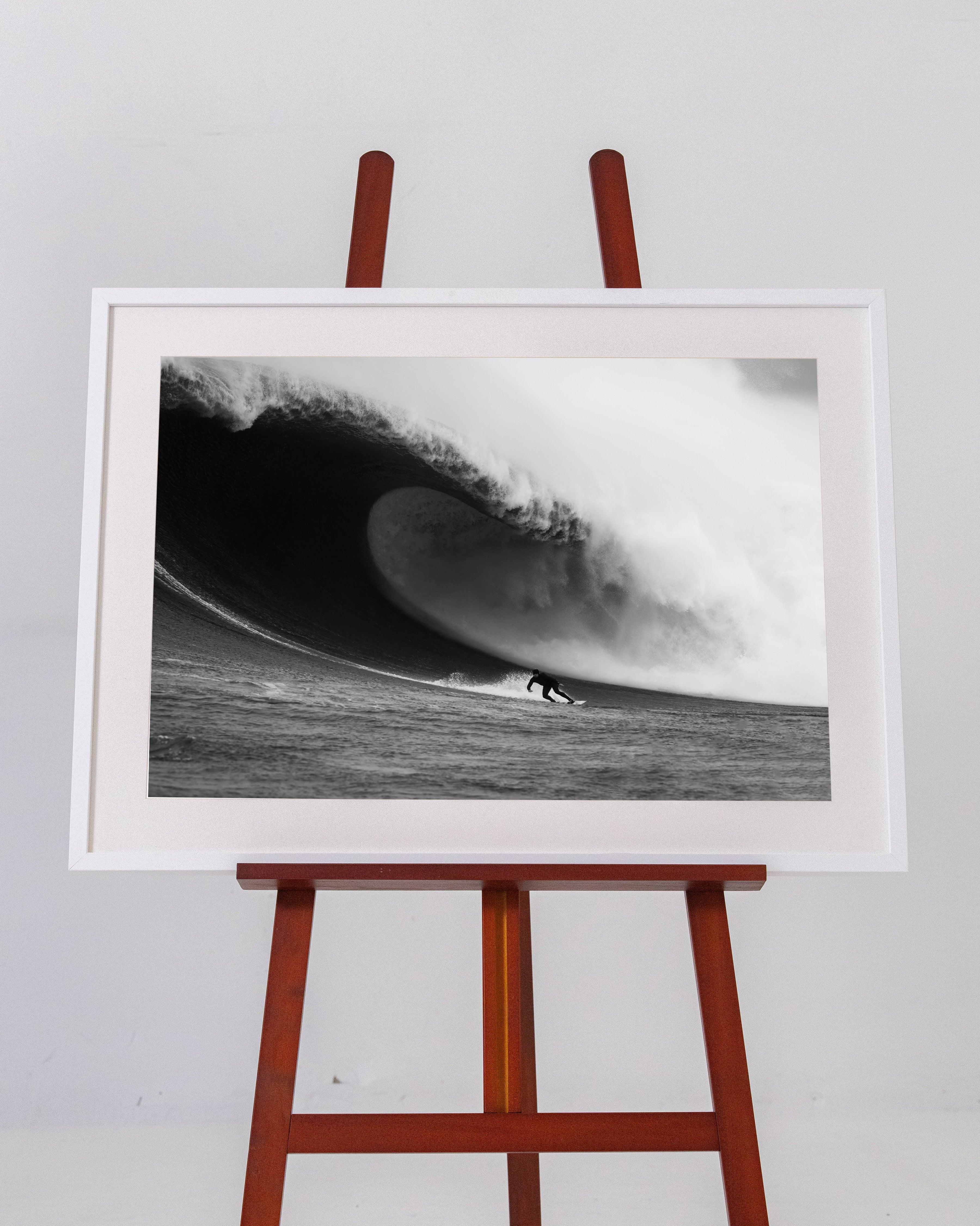 Black and white framed photo of a surfer riding a large, powerful ocean wave on wooden easel