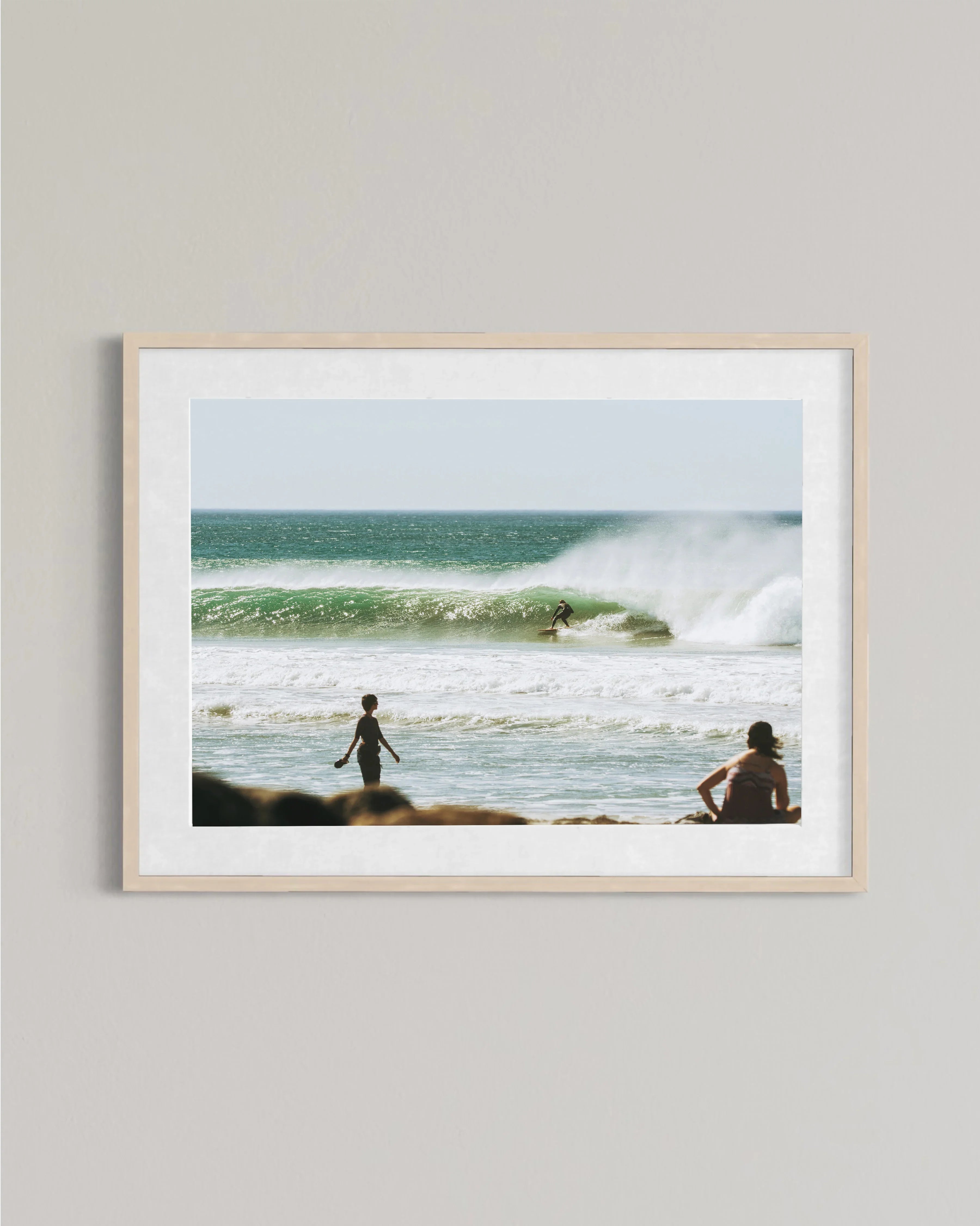 Framed photo of surfer riding wave with two people watching from shore on sunny beach