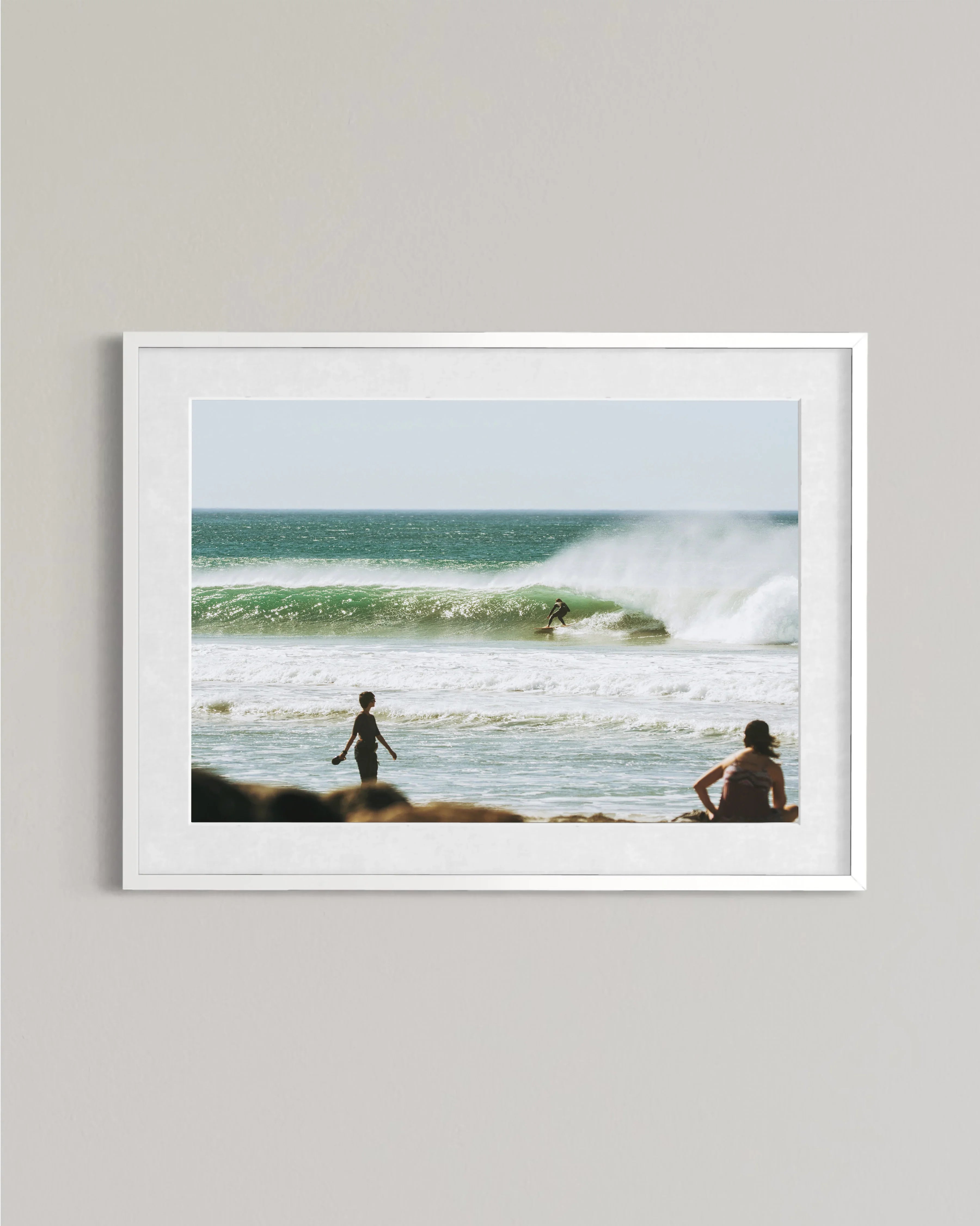 Framed photo of surfer riding green wave with two people watching on the beach
