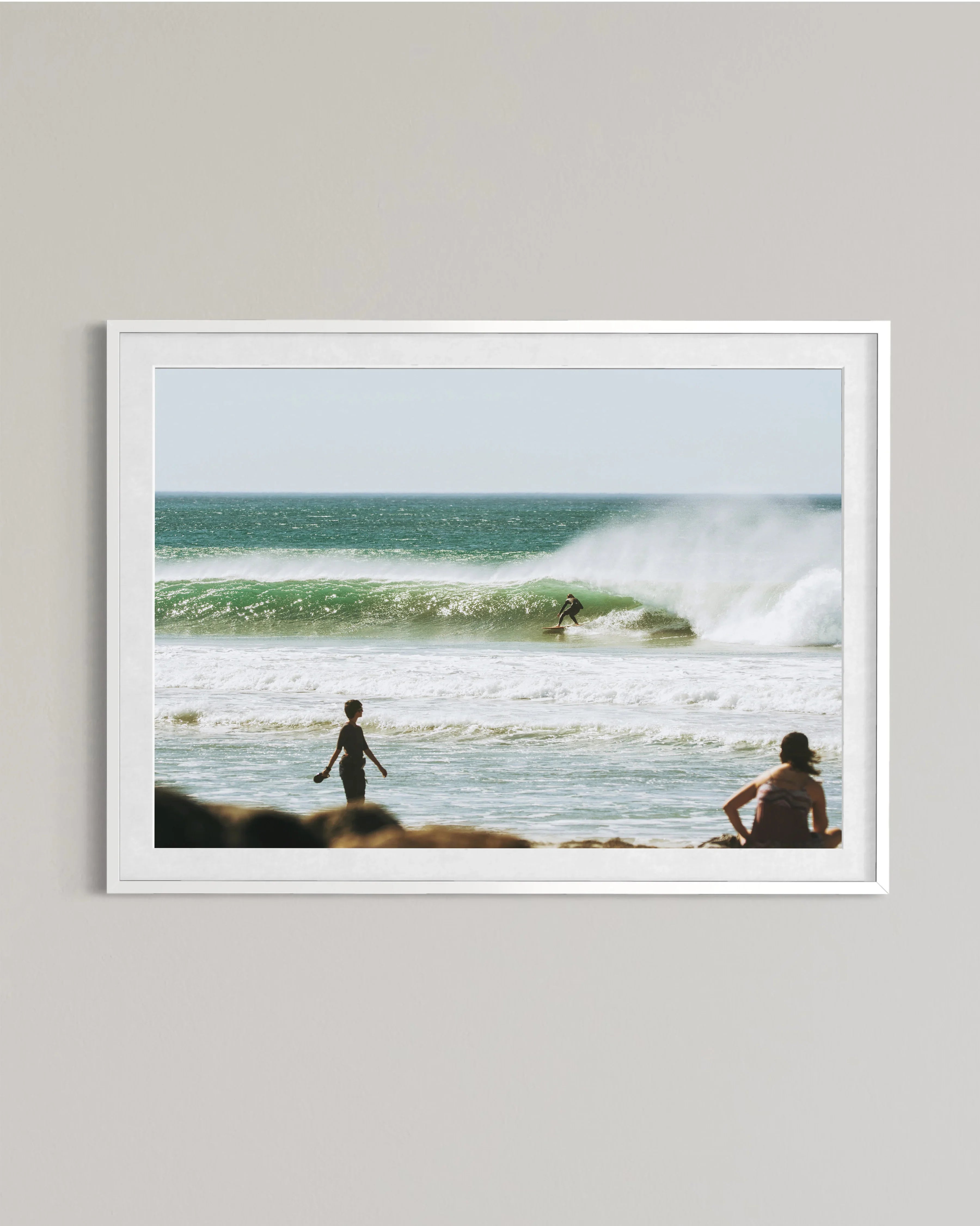 framed photo of surfer riding green wave while two people watch on beach