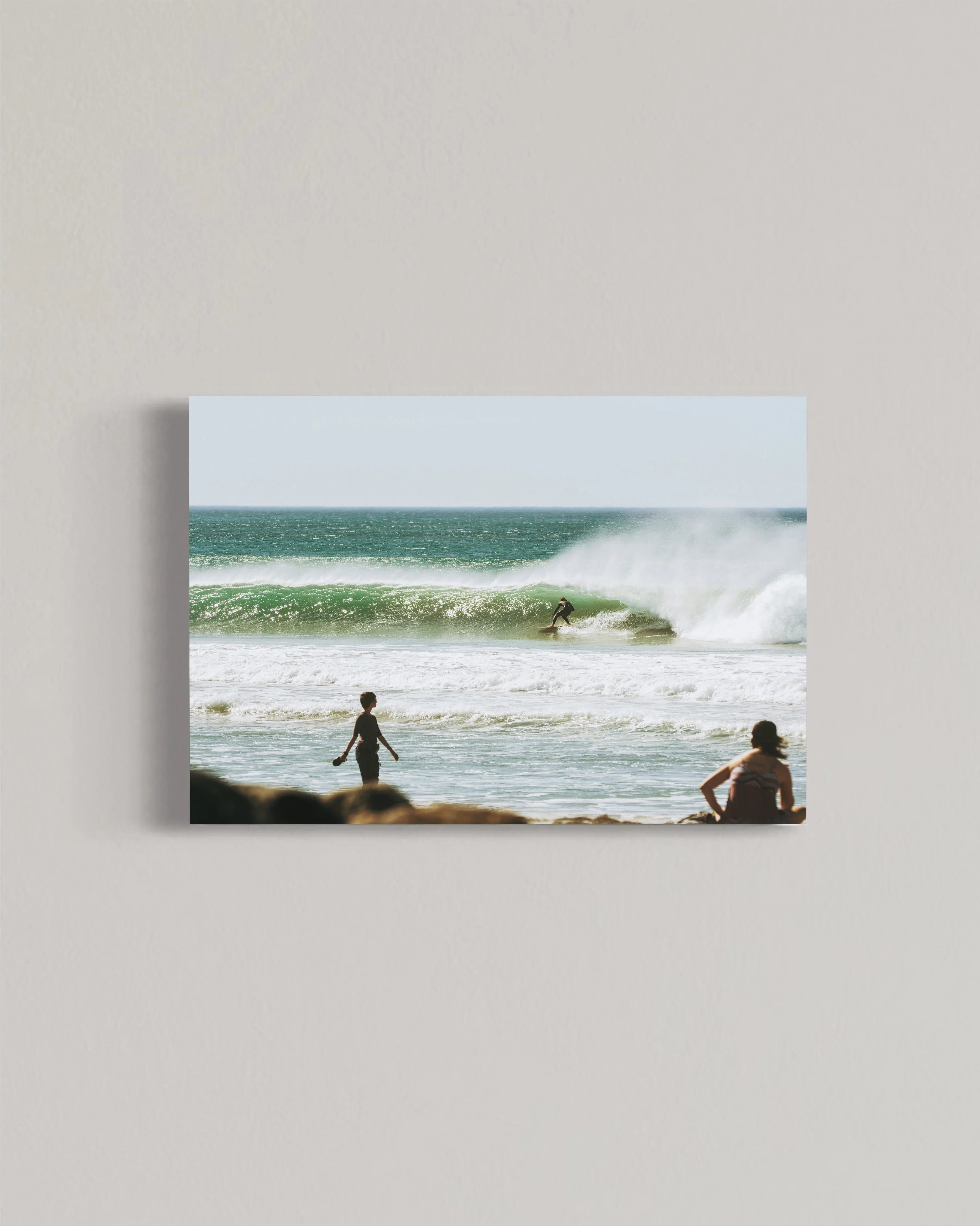 Surfer riding a large green wave with two people watching on the beach in sunny coastal scene