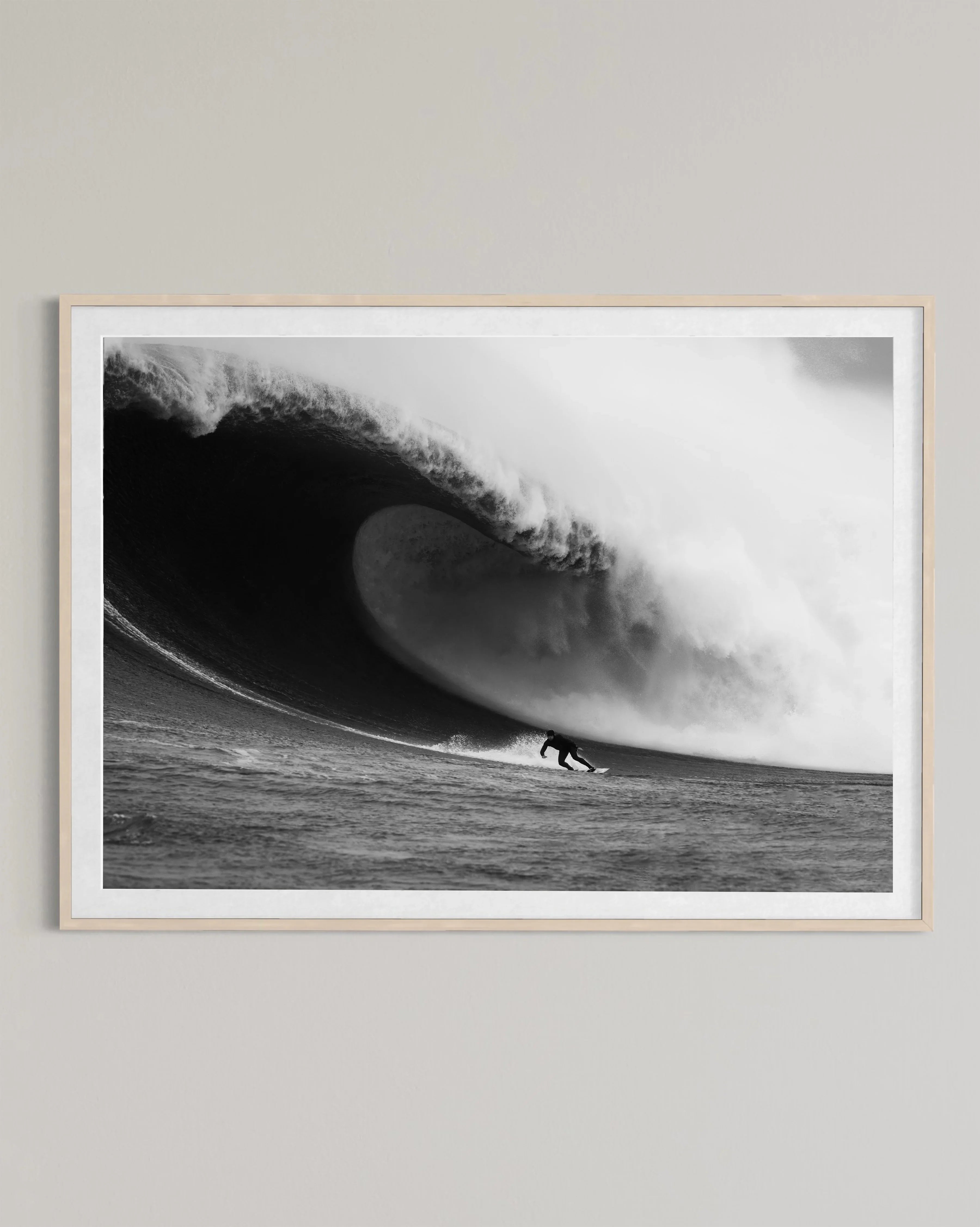 Black and white framed photo of surfer riding a massive curling ocean wave