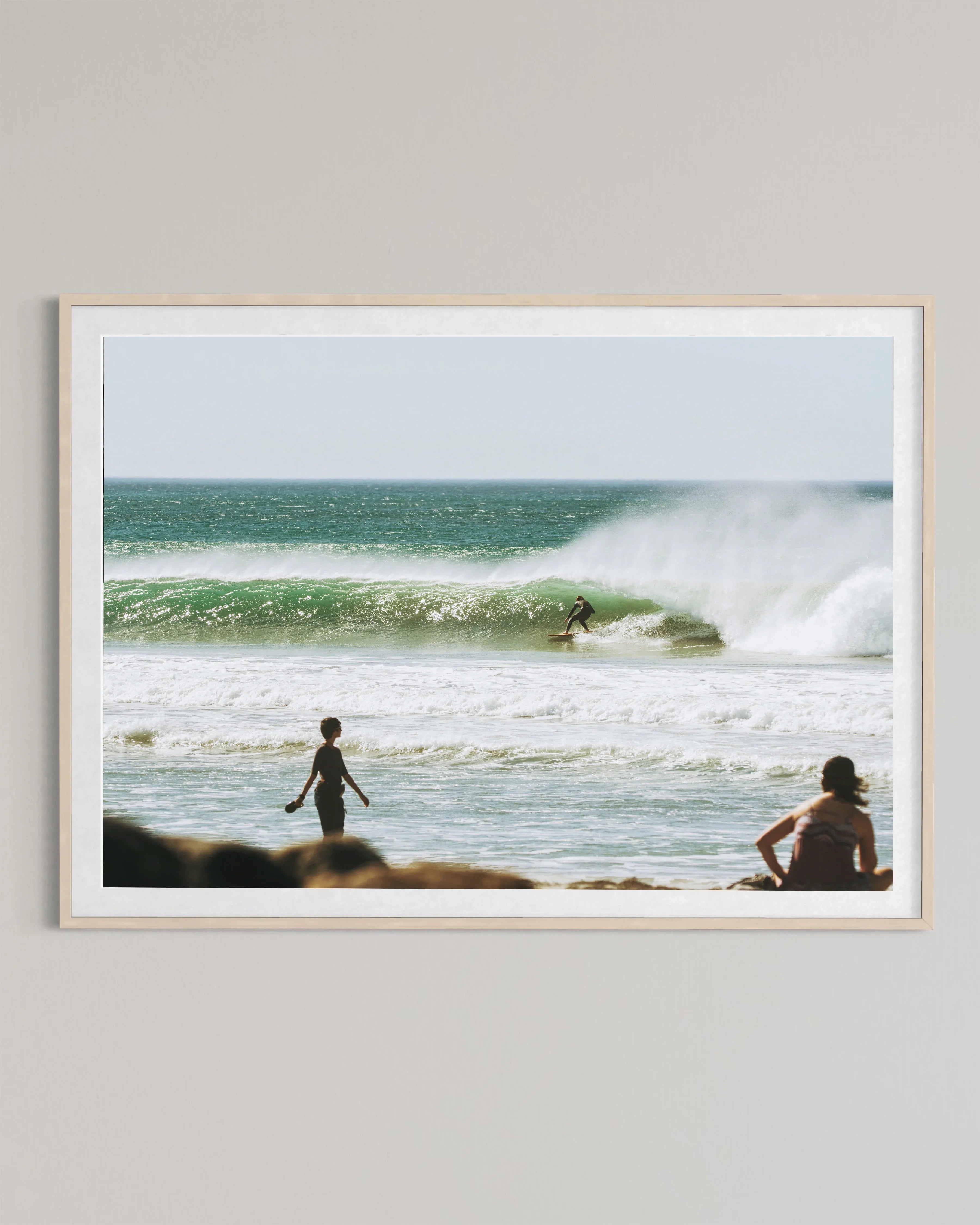 Framed photo of surfer riding large wave with two people watching on sandy beach
