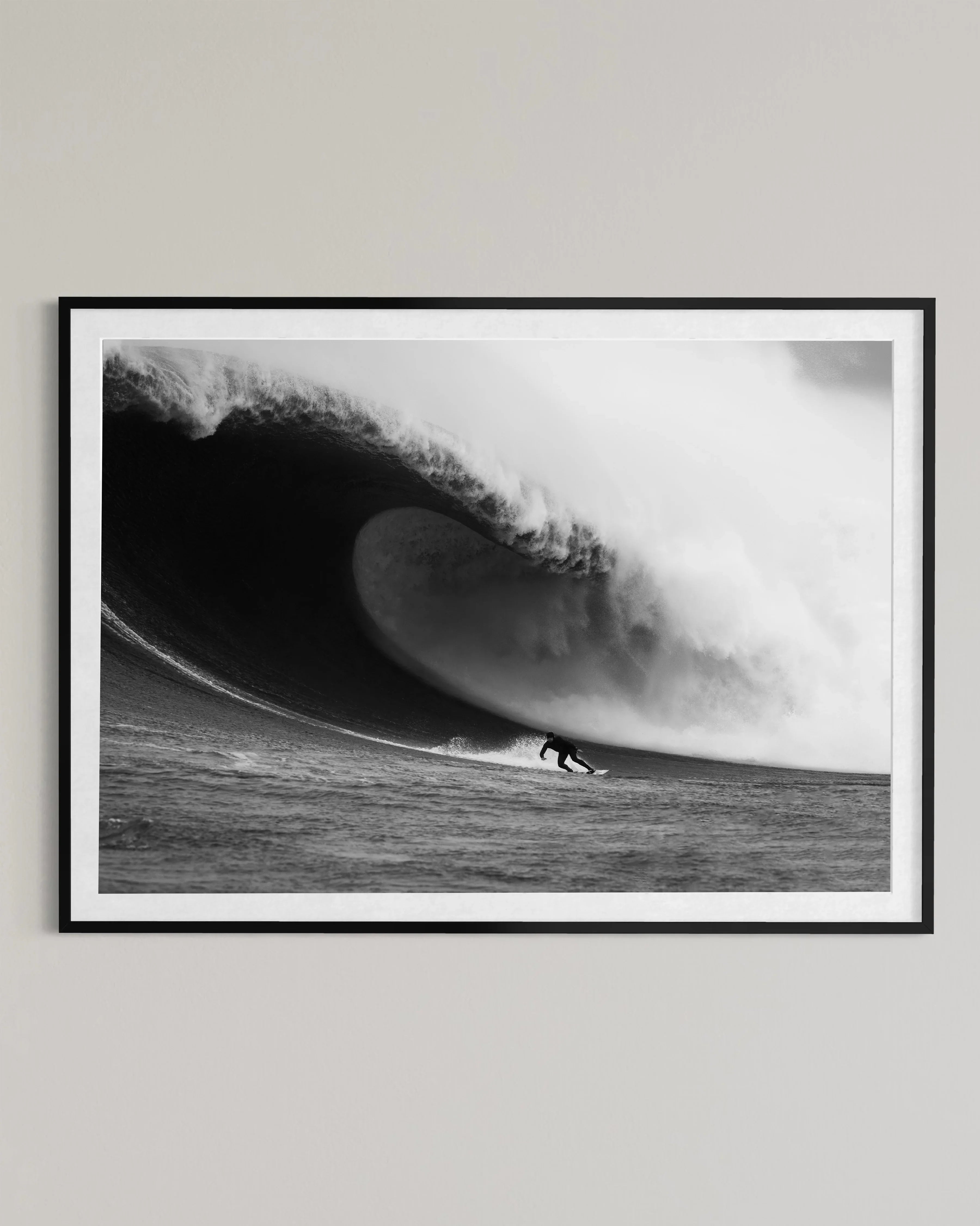 Black and white framed photo of a surfer riding a giant curling wave in the ocean