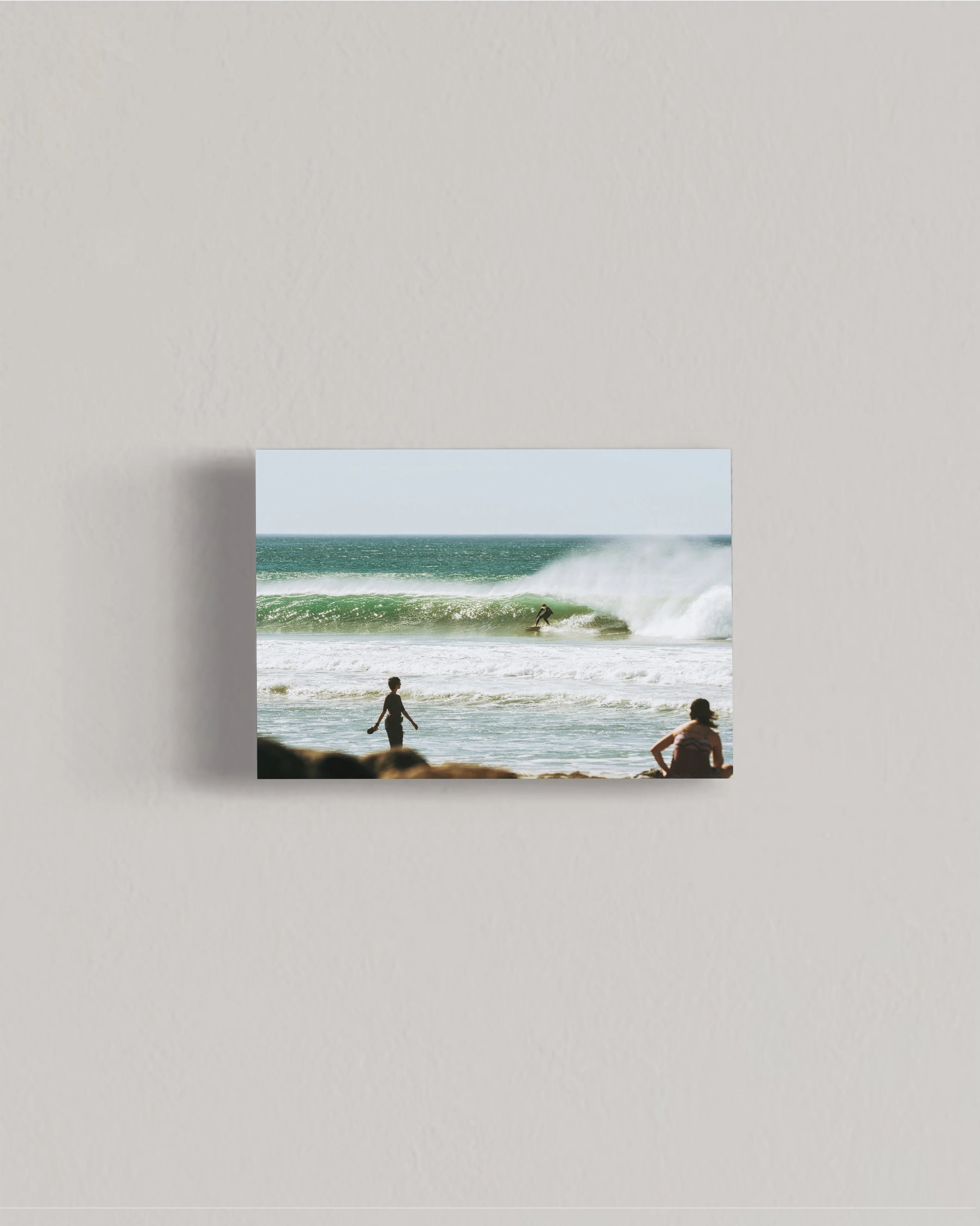 Surfer riding green wave at sunny beach with two people watching from shore