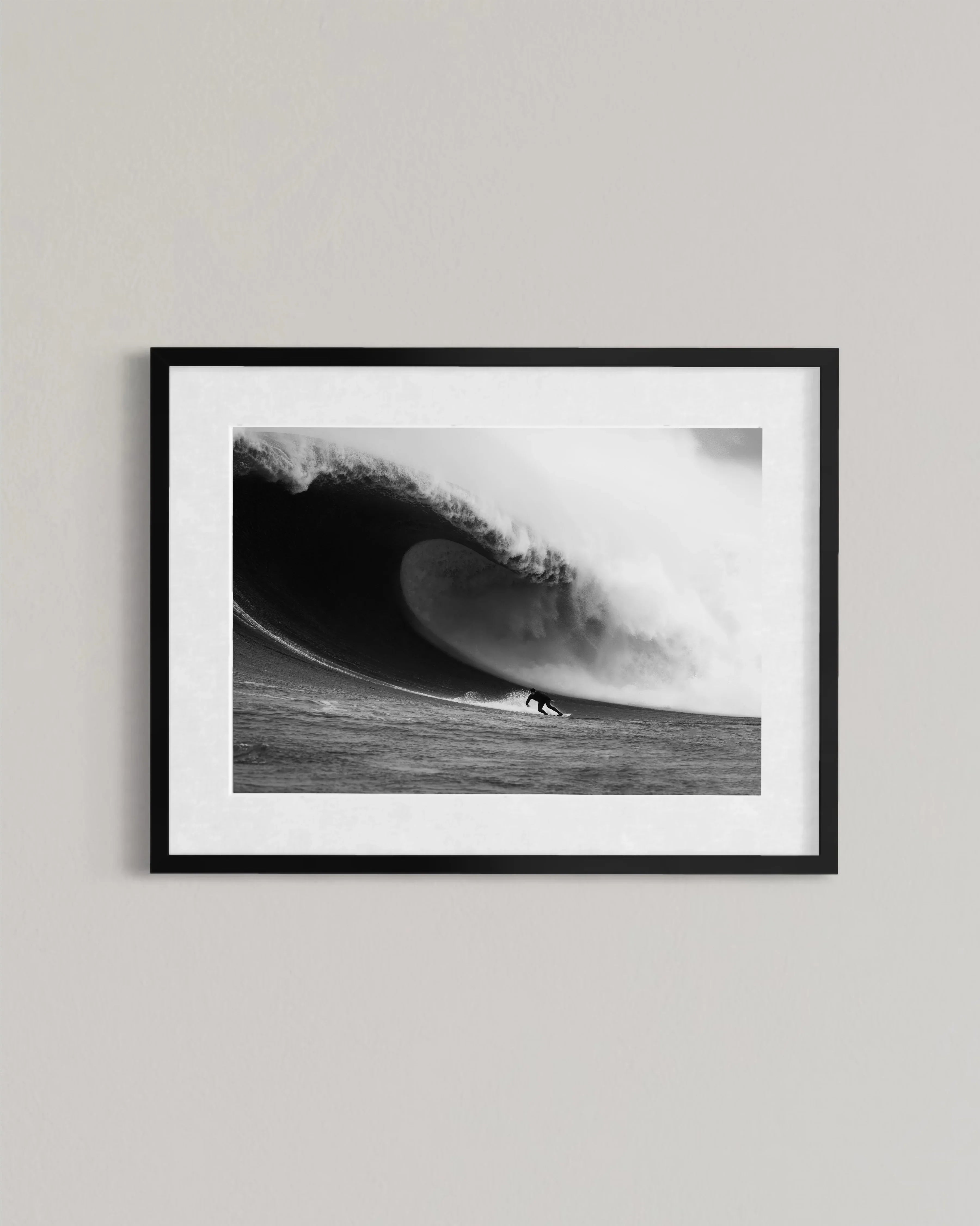 Black and white framed photo of a surfer riding a large curling wave on ocean water