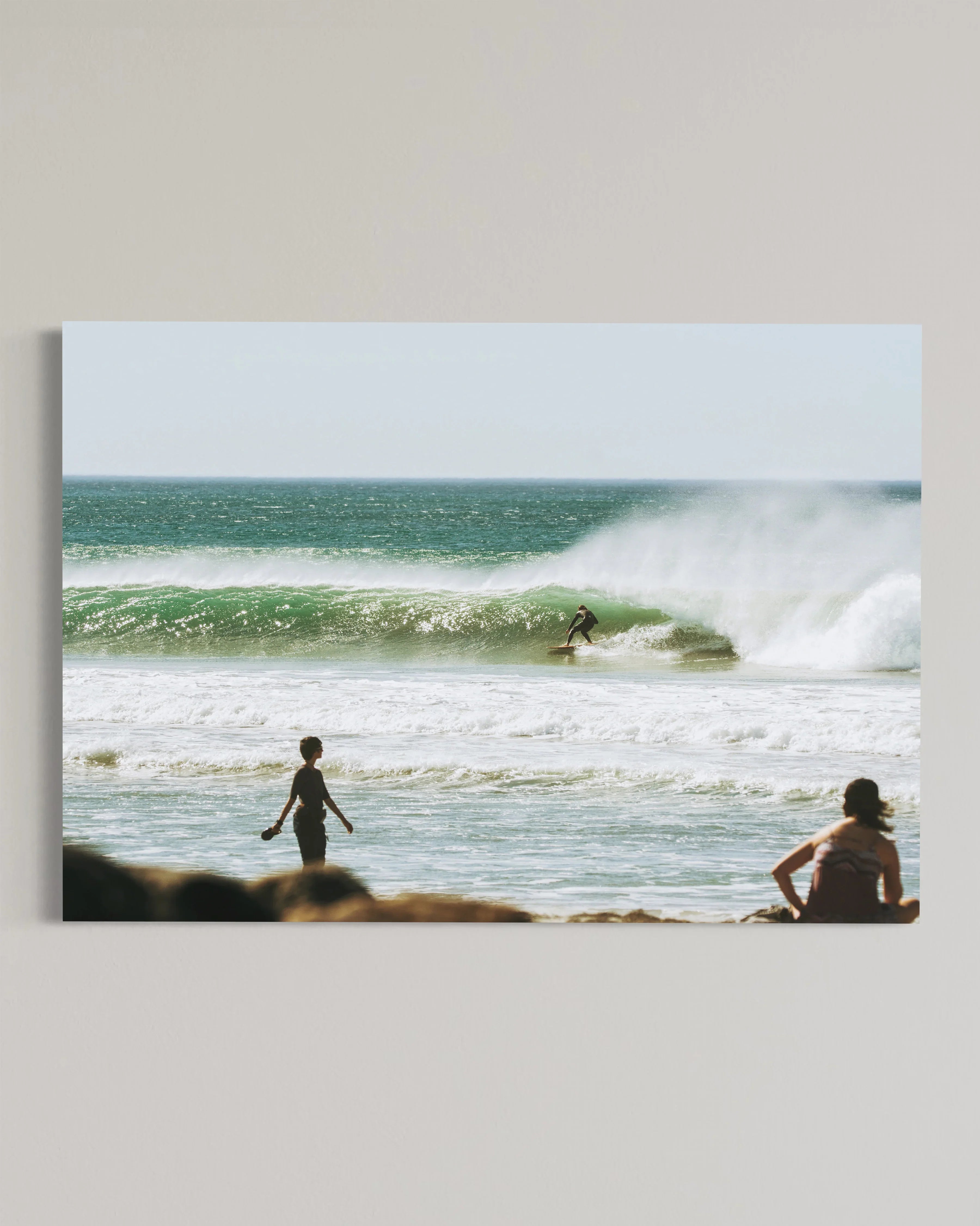 Surfer riding a large wave in the ocean with two people watching from the shore