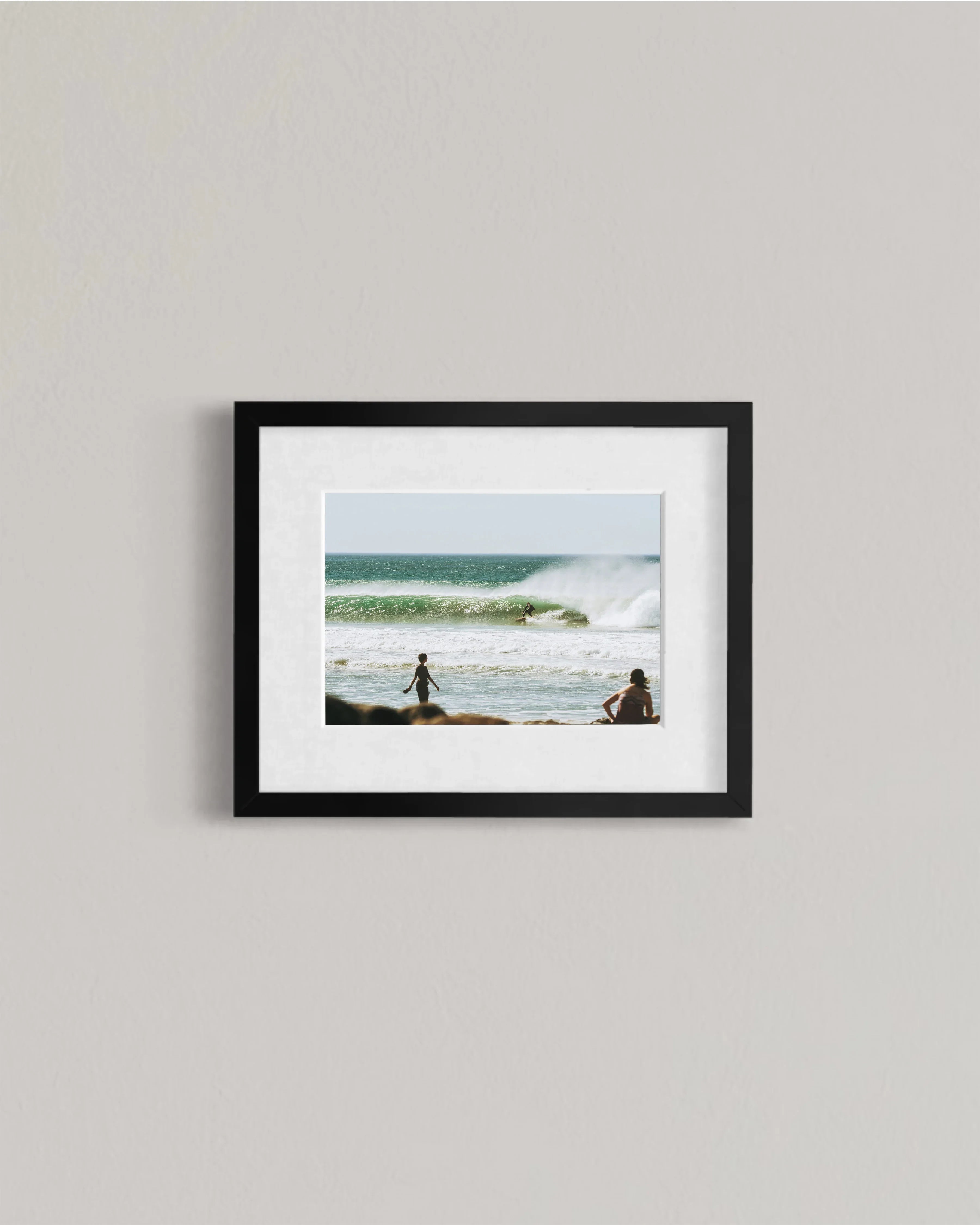 Framed photo of a surfer riding a wave with two people watching on a sunny beach