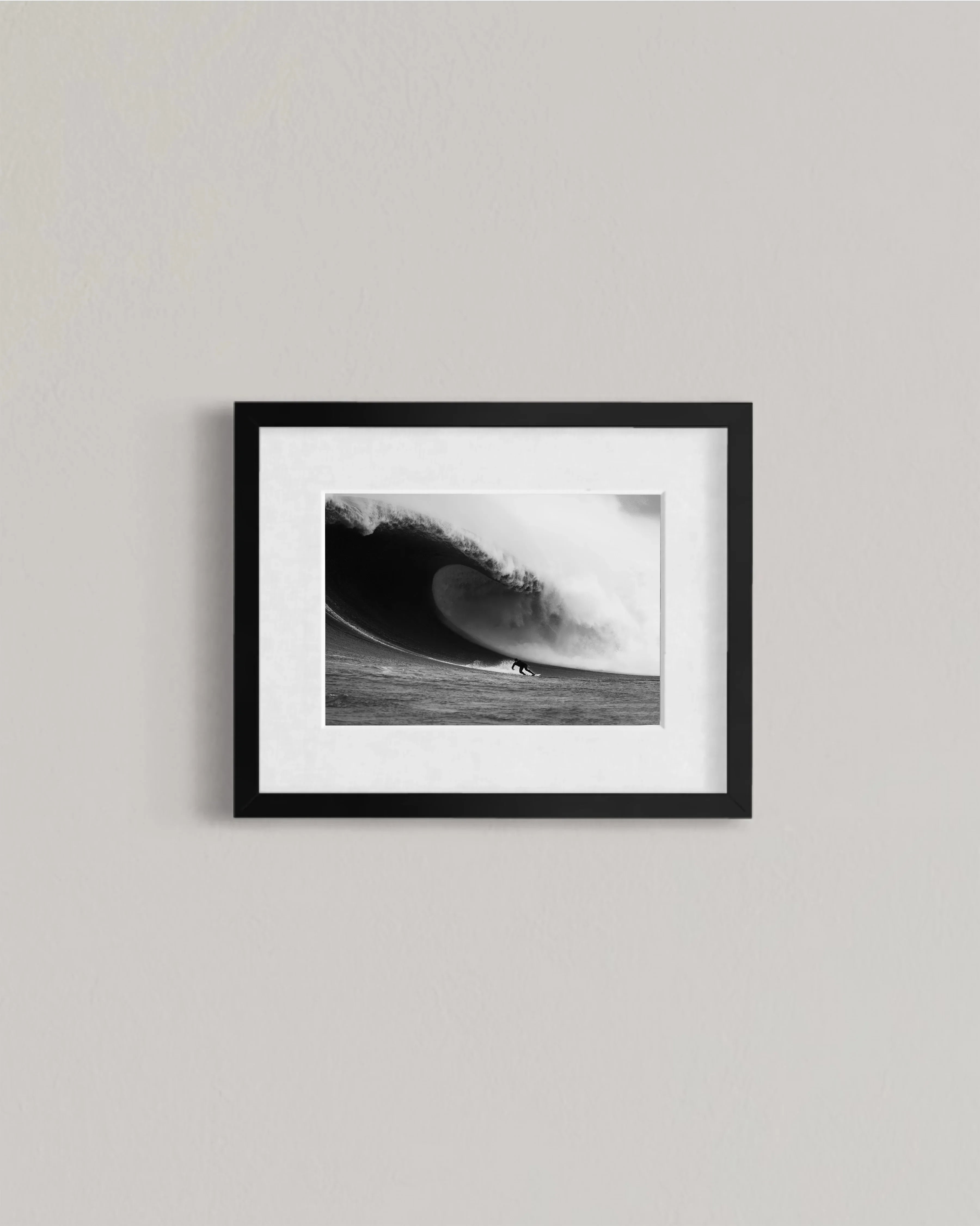 Black and white framed photo of surfer riding a large ocean wave on a gray wall