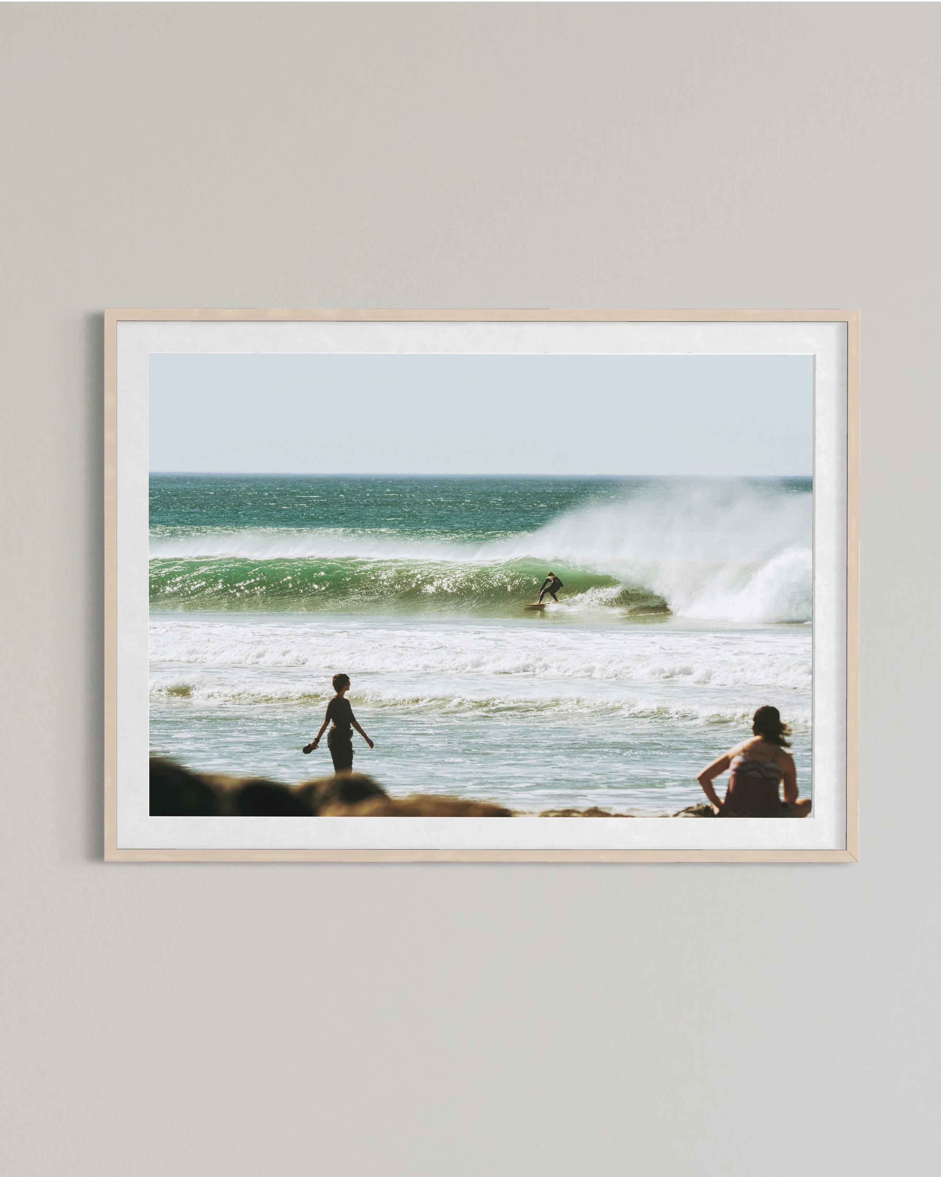 Framed photo of a surfer riding a green wave with two people watching on the beach shore