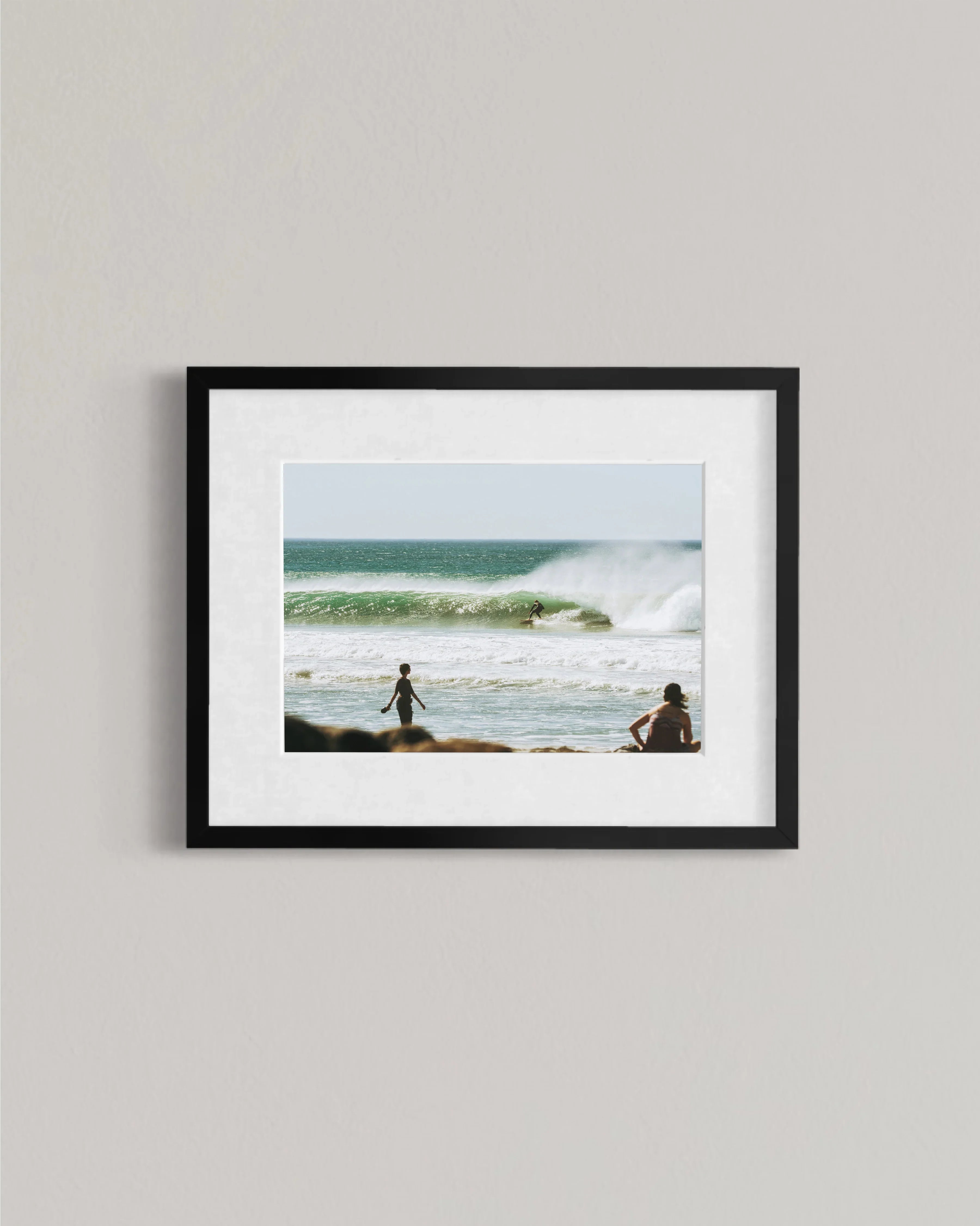 Framed photo of surfer riding wave with ocean and two people on beach in foreground