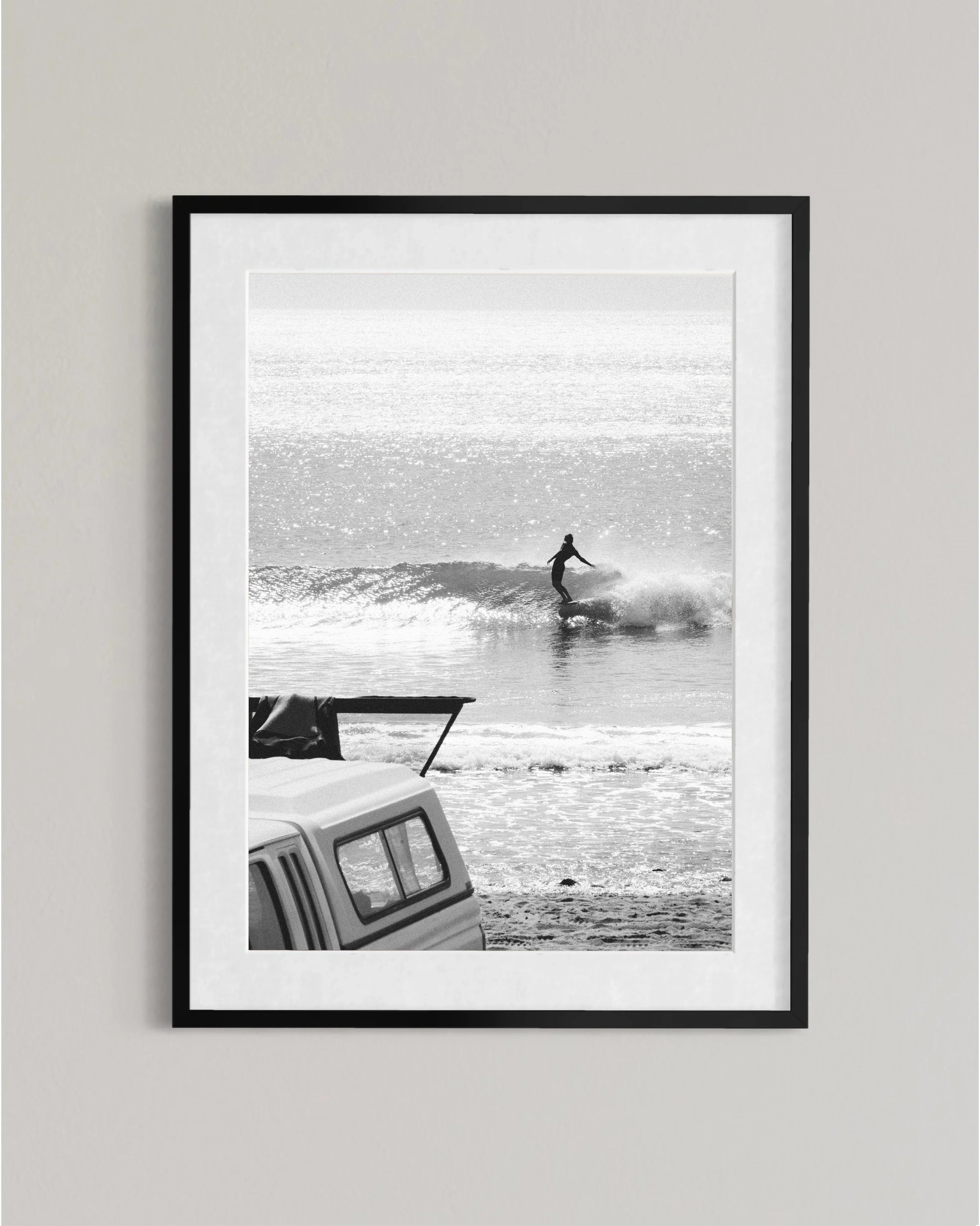 Black and white photo of a surfer riding a wave with a pickup truck on the shore